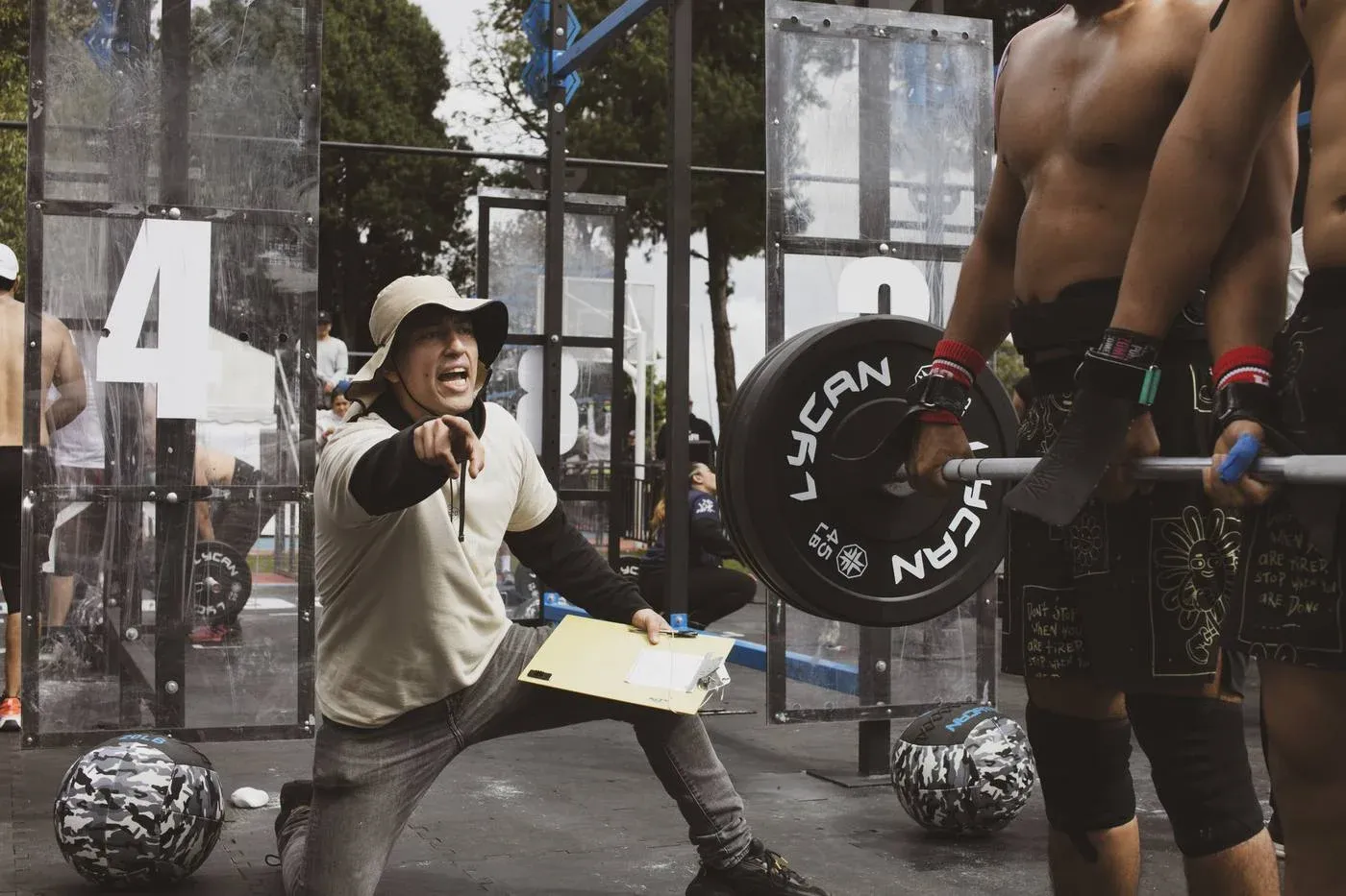 Juez animando a dos atletas que sostienen una barra durante una competencia de CrossFit